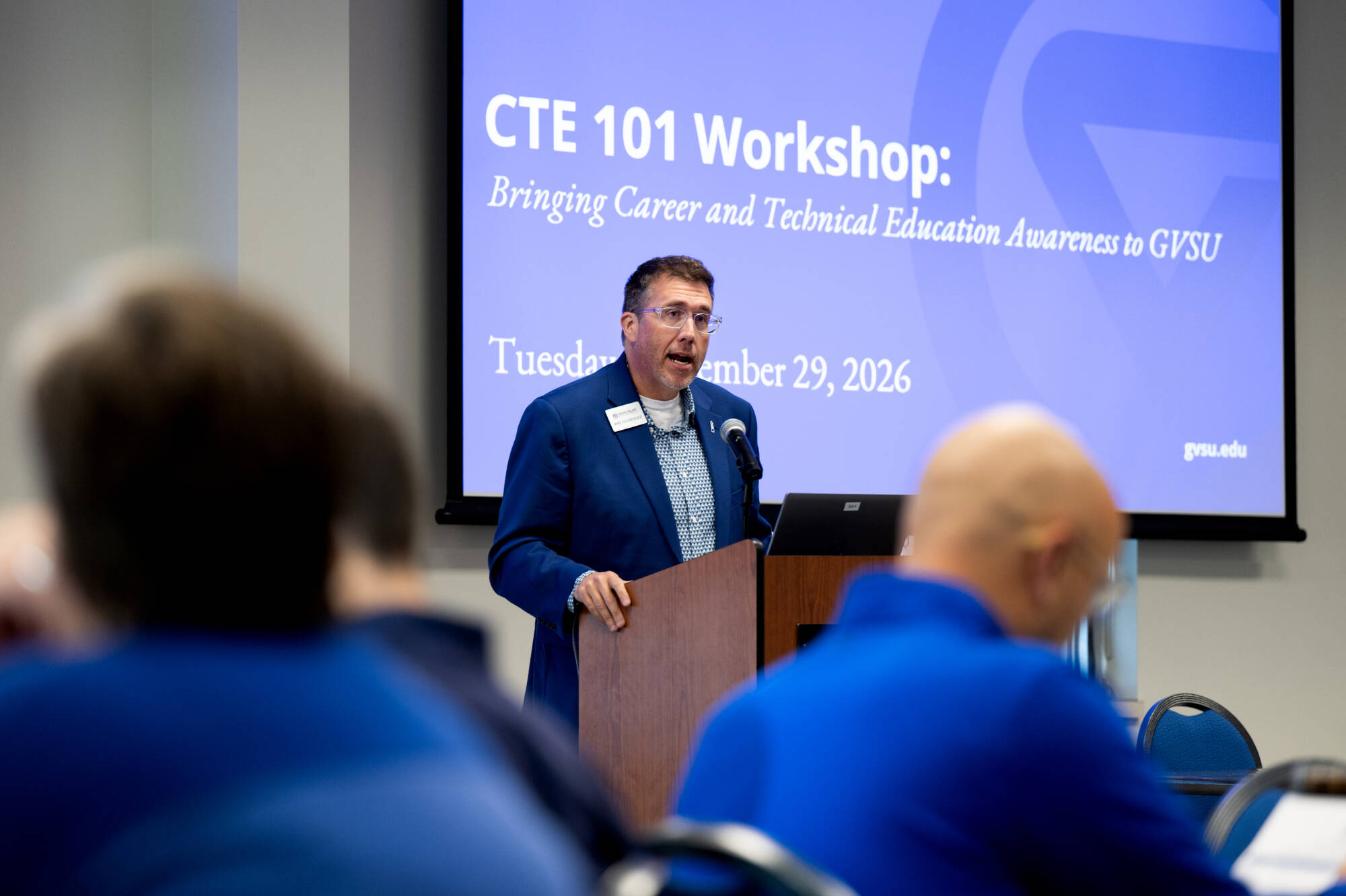Mike Eichberger stands at podium giving remarks, CTE 101 Workshop on screen in background